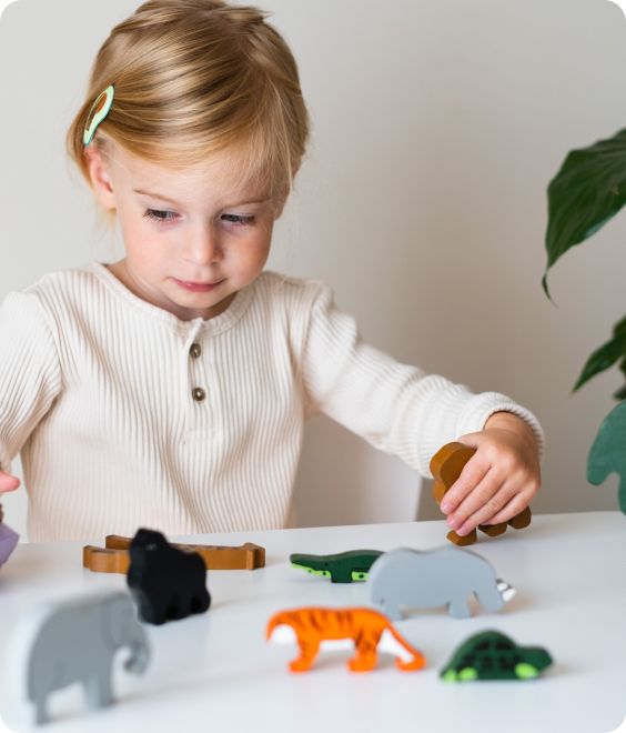 Young child playing with wooden animal toys on a white table