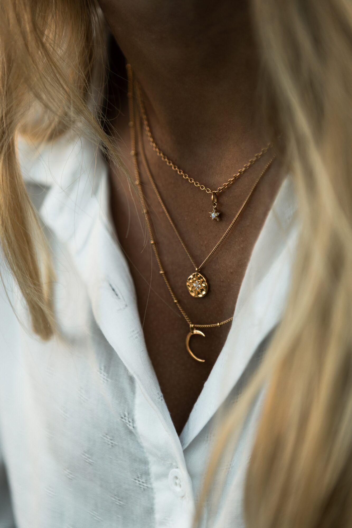Layered gold necklaces worn with an open white shirt